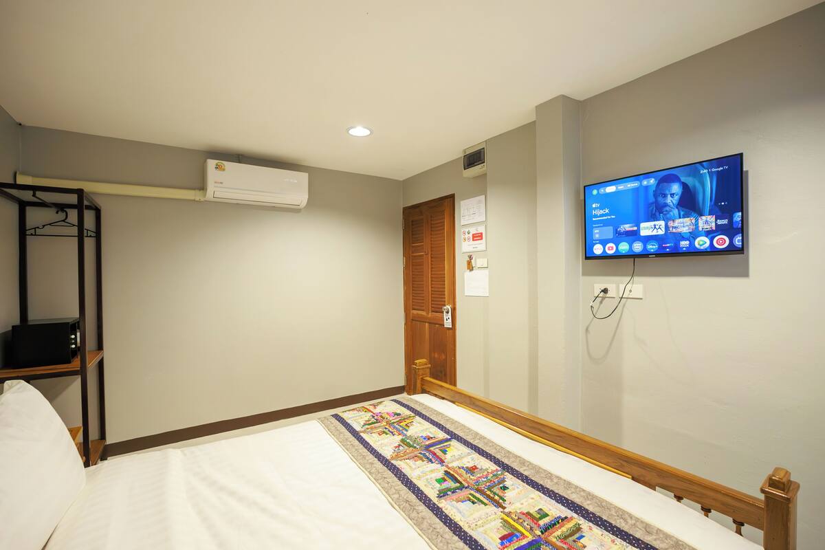 Une chambre d’hôtel équipée d’un lit, d’un téléviseur fixé au mur, d’une porte en bois et d’un appareil de climatisation.