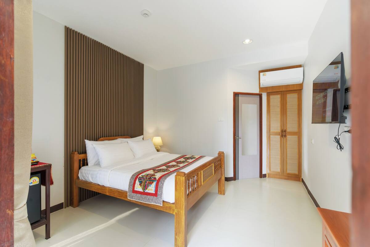 Une chambre à coucher avec un lit en bois, une table de chevet, un téléviseur fixé au mur et une armoire.