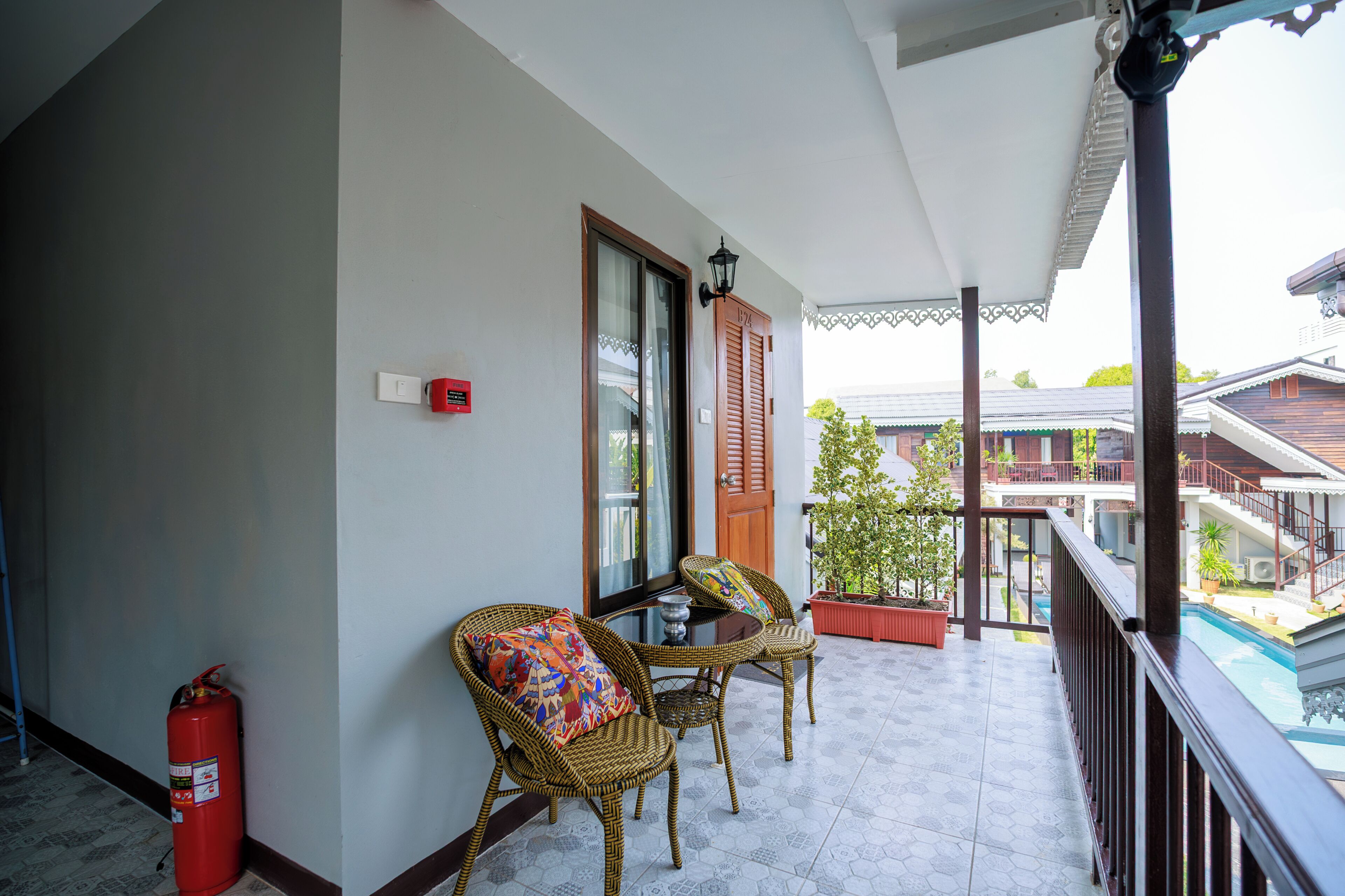 A balcony with wicker chairs, a fire extinguisher, and a door with a window.