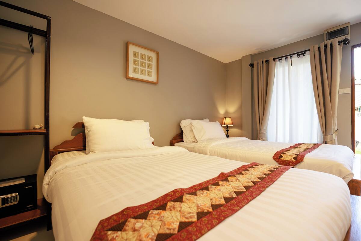 Une chambre d’hôtel avec deux lits, une table de chevet, une lampe, un tableau encadré au mur et une fenêtre avec des rideaux.