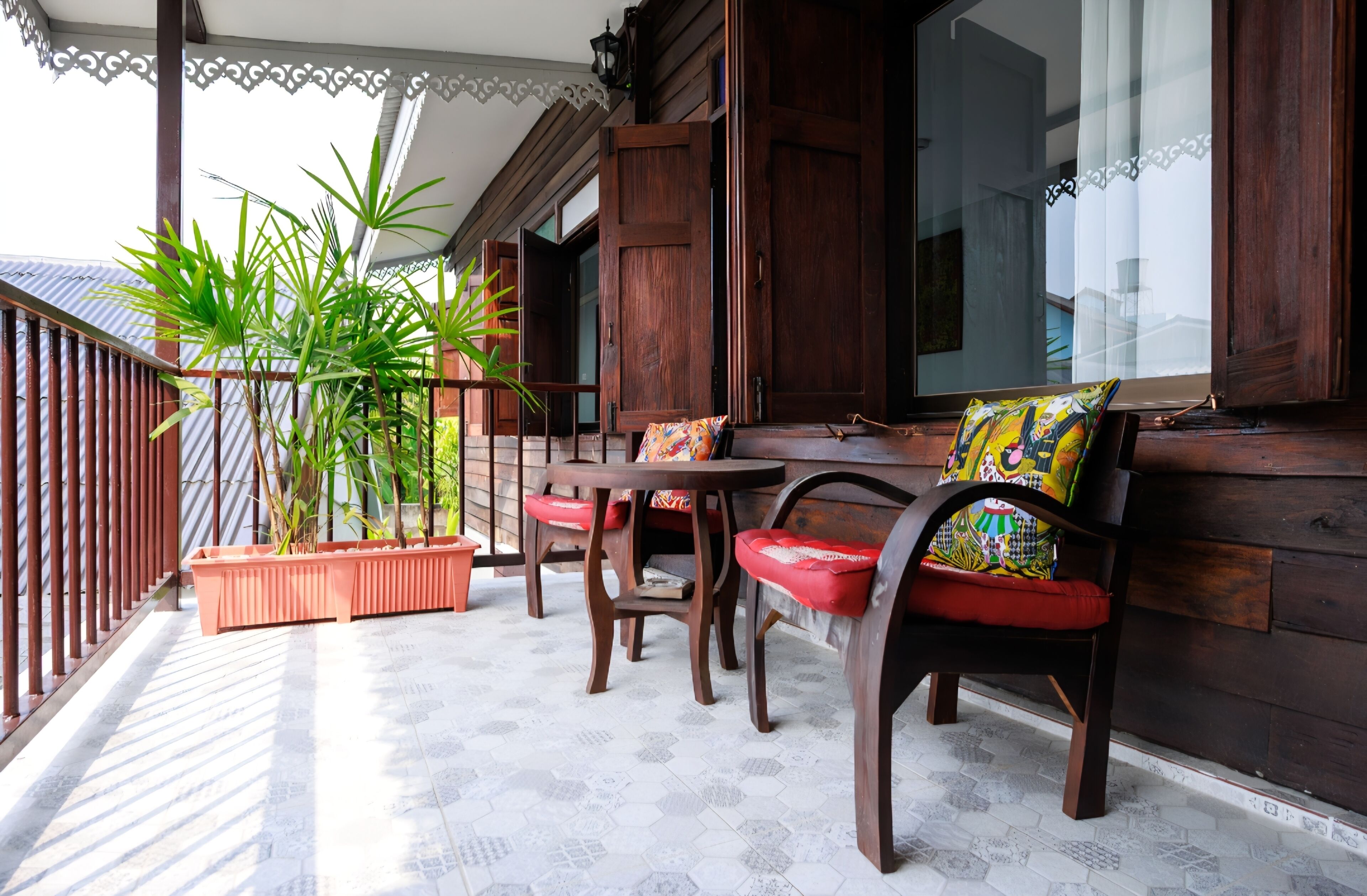 Un porche de madera con una mesa y sillas, plantas en macetas y vistas al interior.