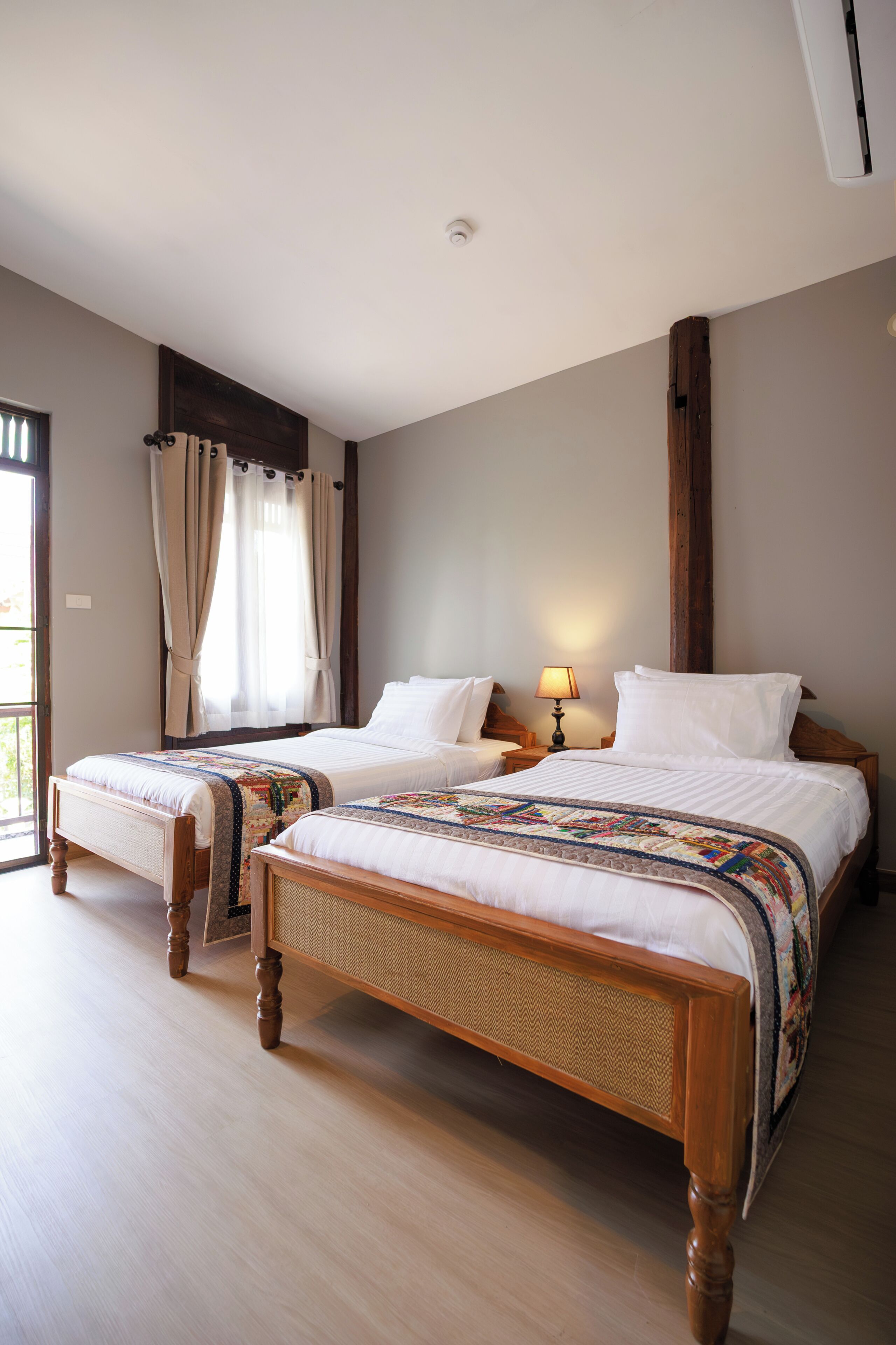 A double bed with a wooden frame and a headboard, a bedside table with a lamp, and a window with curtains.