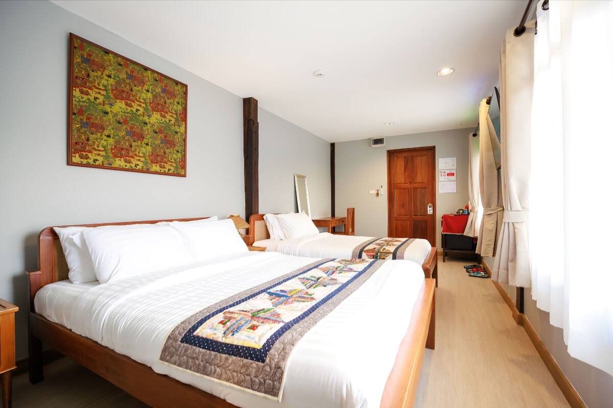 Une chambre d’hôtel avec deux lits, un grand tableau au mur, une porte en bois et une fenêtre avec des rideaux.
