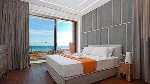 A modern hotel room with a large bed, a wooden nightstand, and a view of the ocean. - Suncity Icon - Luxury Beachfront Villa (Ayia Napa)