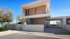 A modern two-story building with a flat roof, a large entrance, and a view of the sea. - Suncity Icon - Luxury Beachfront Villa (Ayia Napa)