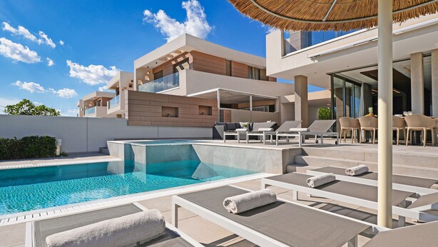 A modern pool area with lounge chairs and a thatched umbrella. - Suncity Icon - Luxury Beachfront Villa (Ayia Napa)