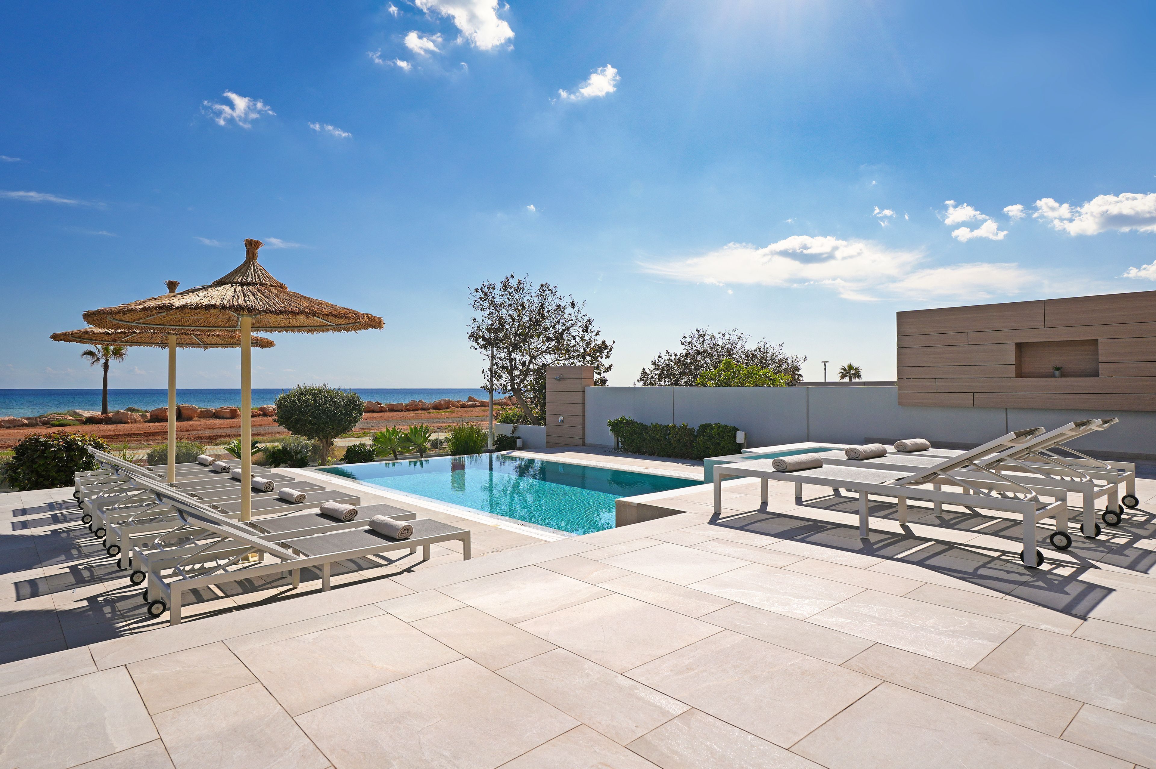 A rooftop pool area with lounge chairs, a thatched umbrella, and a view of the sea.