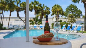 Une table placée au bord de la piscine, avec une bouteille de vin, un verre et un bol de crackers.