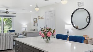 Une cuisine moderne avec un plan de travail en marbre, un vase de fleurs et un coin repas avec des chaises bleues.