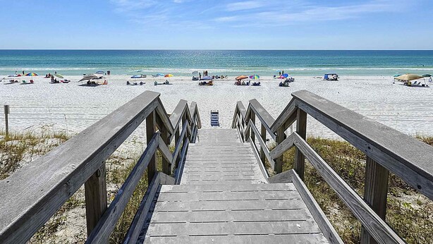 Une promenade en bois menant à une plage où se trouvent des parasols et des gens.