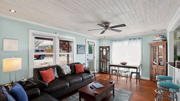 A living room with a black leather sofa, a wooden coffee table, a ceiling fan, and a dining area with a table and chairs.