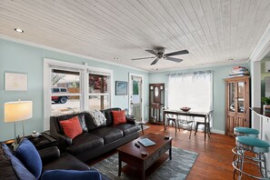 A living room with a black leather sofa, a wooden coffee table, a ceiling fan, and a dining area with a table and chairs.