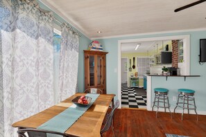 A dining area with a wooden table, chairs, a fruit bowl, and a patterned curtain.