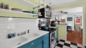 Een keuken met witte en blauwe kastjes, een zwart-wit geruite vloer, een magnetron en een spoelbak.