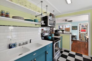 A kitchen with white and blue cabinets, a black and white checkered floor, a microwave, and a sink.