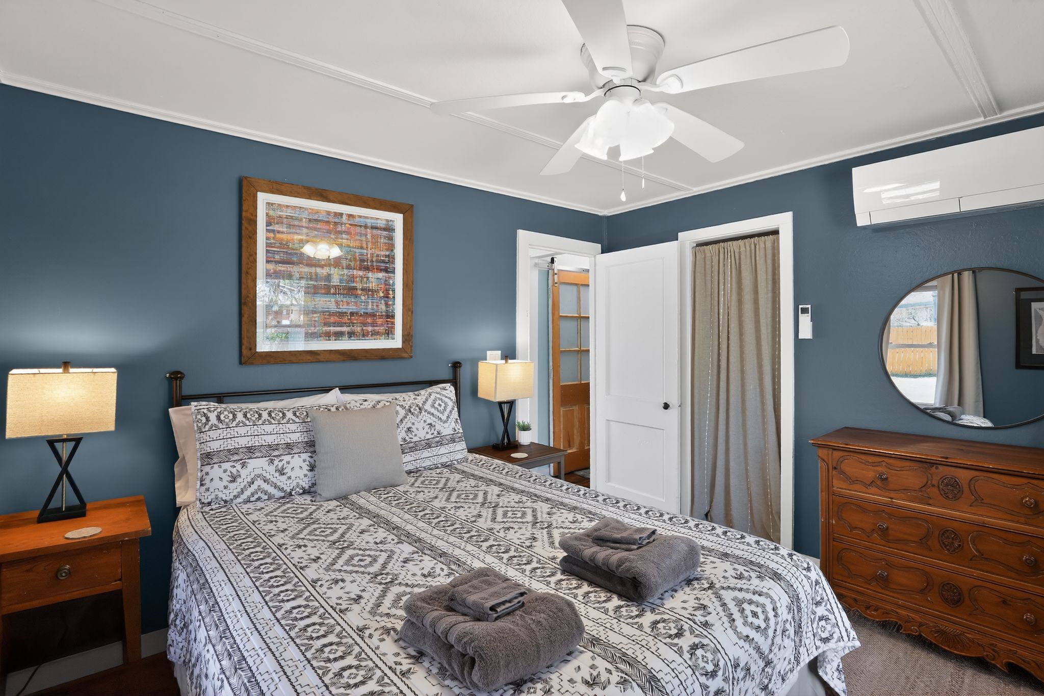 A bedroom with a bed, a nightstand, a dresser, a ceiling fan, a framed picture, and a door.