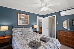 A bedroom with a bed, a nightstand, a dresser, a ceiling fan, a framed picture, and a door.