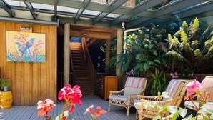 Une terrasse en bois agrémentée de meubles en osier, d’un escalier et d’une végétation luxuriante.