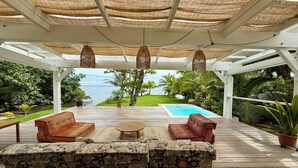 Ein überdachter Außenbereich mit Pool, Liegestühlen und Blick auf den Ozean.