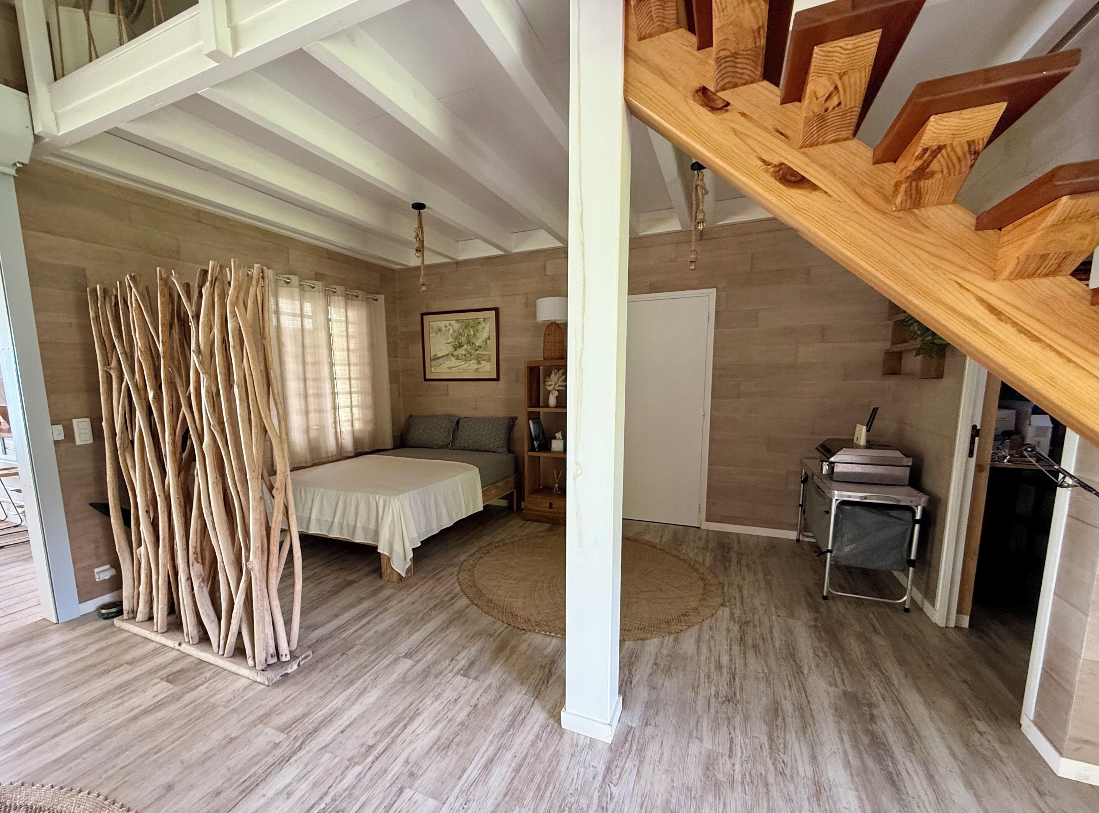 Une pièce spacieuse comprenant un lit, un plancher en bois, un escalier et une porte donnant sur une autre pièce.