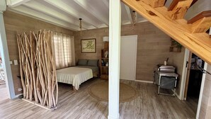 Ein geräumiger Raum mit einem Bett, Holzboden, einer Treppe und einer Tür zu einem weiteren Raum.