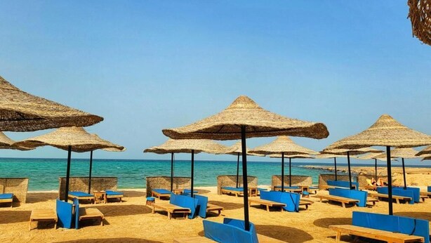 Een strand met houten ligbedden en rieten parasols.