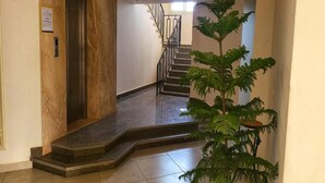 Een hal met een marmeren muur, een trap en een kamerplant.