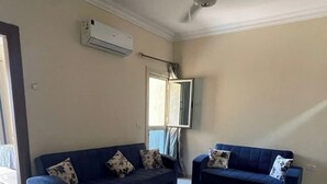 Een woonkamer met twee donkerblauwe banken, een tapijt met patroon, een plafondventilator en een airconditioner.