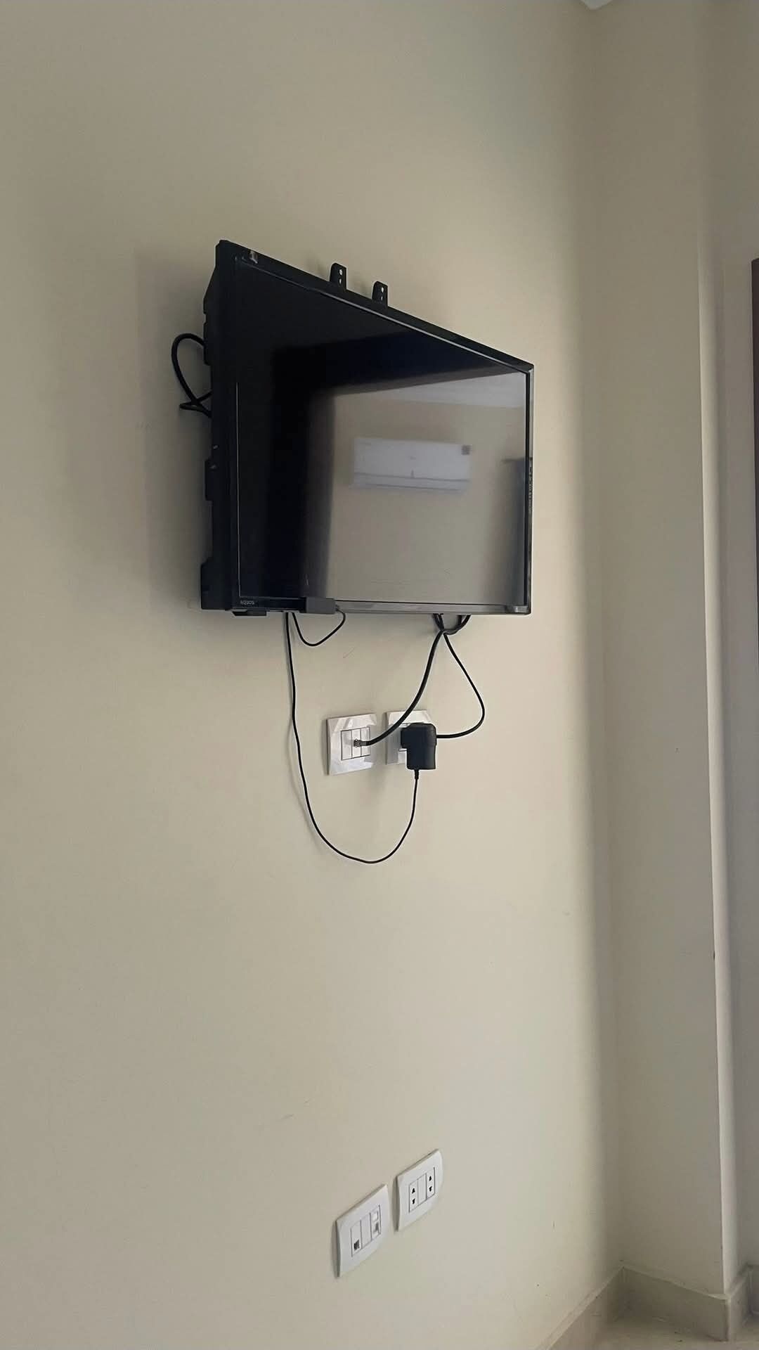 Een televisie bevestigd aan een muur, met een stroomkabel aangesloten op een stopcontact.