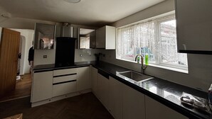 Una cocina con armarios blancos, encimera negra y una ventana con cortinas decorativas.