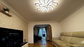 Una sala de estar con televisor de pantalla plana, sofá de cuero, piso de madera y una lámpara decorativa en el techo.