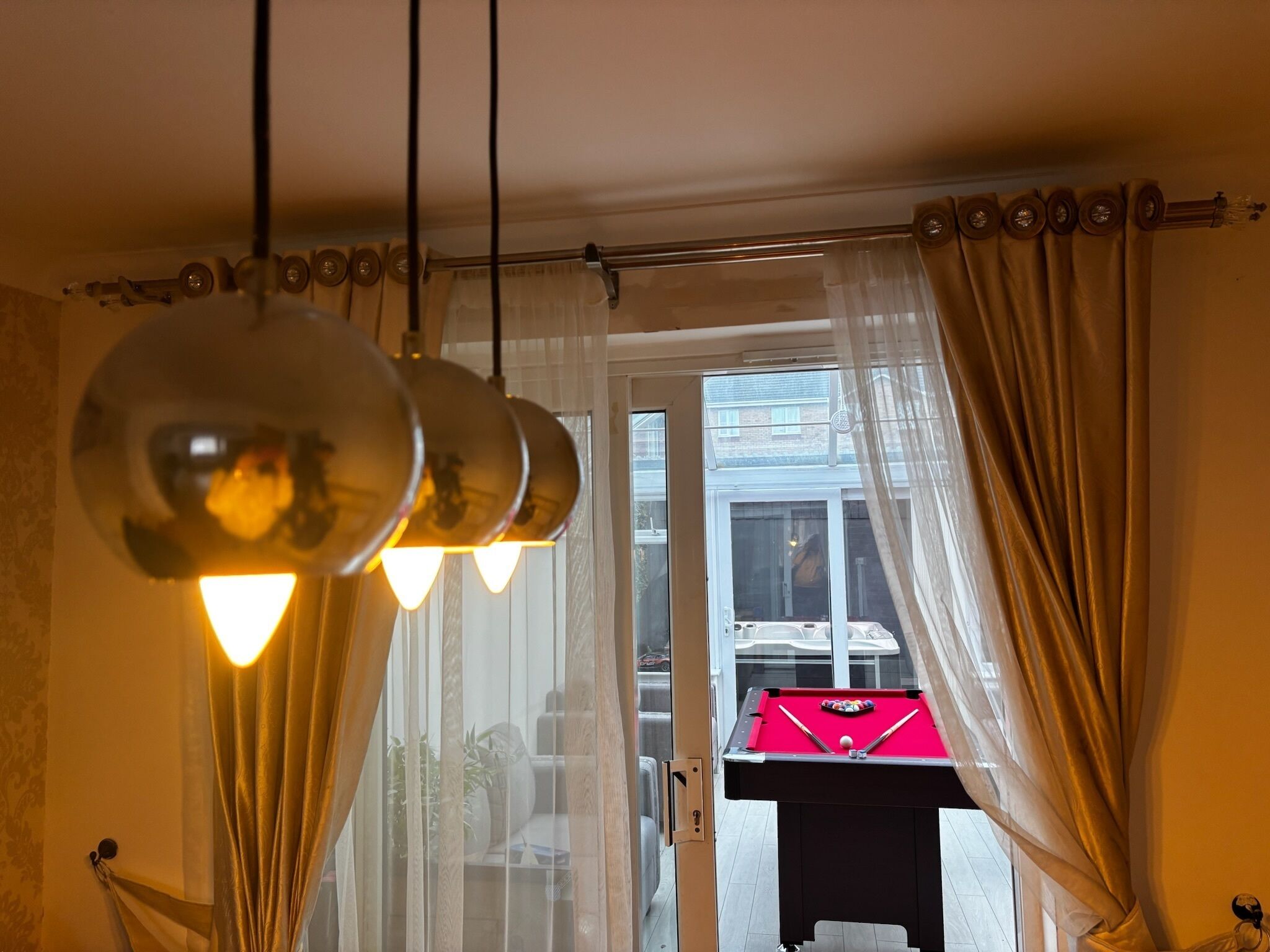 A room with a pool table, a hanging light fixture, and sheer curtains.