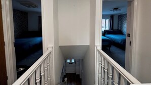 Pasillo que conduce a dos dormitorios con paredes blancas y una escalera.