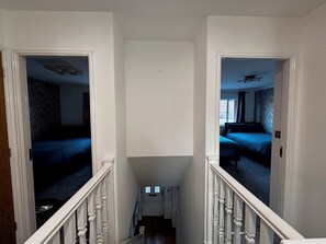 A hallway leading to two bedrooms with white walls and a staircase. - Semi Detached City Retreat - Jacuzzi - Pool Table - Driveway Parking (Cardiff)