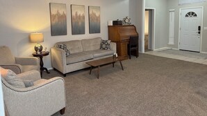 Ein Wohnzimmer mit einer Couch, einem Couchtisch, einer Lampe, einem Klavier und drei Bildern an der Wand.