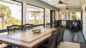 A dining area with a wooden table and chairs, a ceiling fan, and large windows with a view of palm trees. - Oceanfront Home w/ Pool + Private Beach Access (St. Augustine)