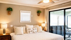 A bedroom with a large bed, two bedside lamps, a ceiling fan, and a view of the outdoors. - Oceanfront Home w/ Pool + Private Beach Access (St. Augustine)