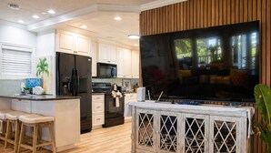 A modern kitchen with a large TV, wooden cabinets, and a bar area with stools. - Oceanfront Home w/ Pool + Private Beach Access (St. Augustine)