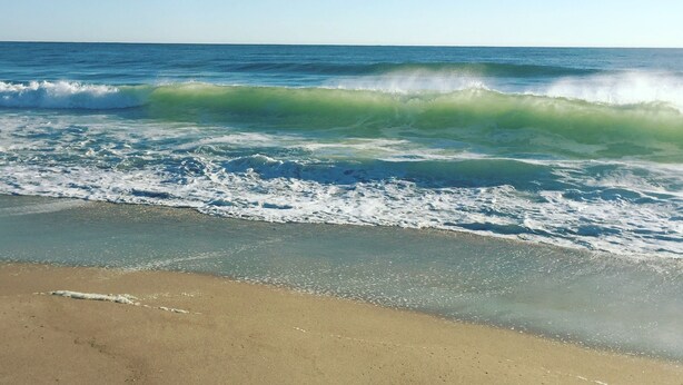 Ein Strand mit Wellen und blauem Himmel.