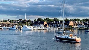 Ein Yachthafen mit vertäuten Booten, ein Segelboot im Vordergrund und eine Stadt mit Gebäuden und einer Kirche im Hintergrund.
