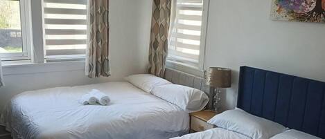A hotel room with two beds, a painting on the wall, and a window with blinds.