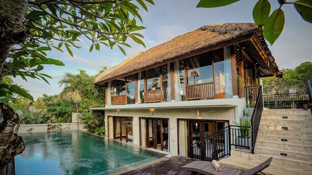 A two-story building with a pool, wooden deck, and a thatched roof. - Villa Campania Bali (Sukawati)