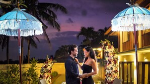 A couple standing under a thatched roof, surrounded by a decorative floral arrangement and candles. - Villa Campania Bali (Sukawati)