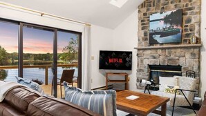 Ein Wohnzimmer mit Kamin aus Stein, einem Fernseher und Blick auf einen See.