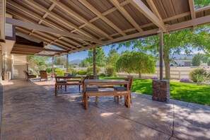 An outdoor patio with stone flooring, wooden furniture, and a covered area with a view of a landscaped garden and distant mountains. - Marbella Lane - Eccentric 4BR Modern Ranch Home (Reno)
