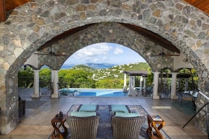 An outdoor seating area with stone arches, a pool, and a view of green hills. - Arc Du Soleil- Ultimate Island Living, Refreshing Salt Water Pool, Stunning Views! (Cruz Bay)