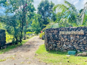 A stone wall with 'TE NUNOA' carved on it, a dirt path, and lush greenery. - Villa - Moorea, Haapiti. 4 bedrooms - sleeps 8 to 12 Ideal for families (Moorea-Maiao)