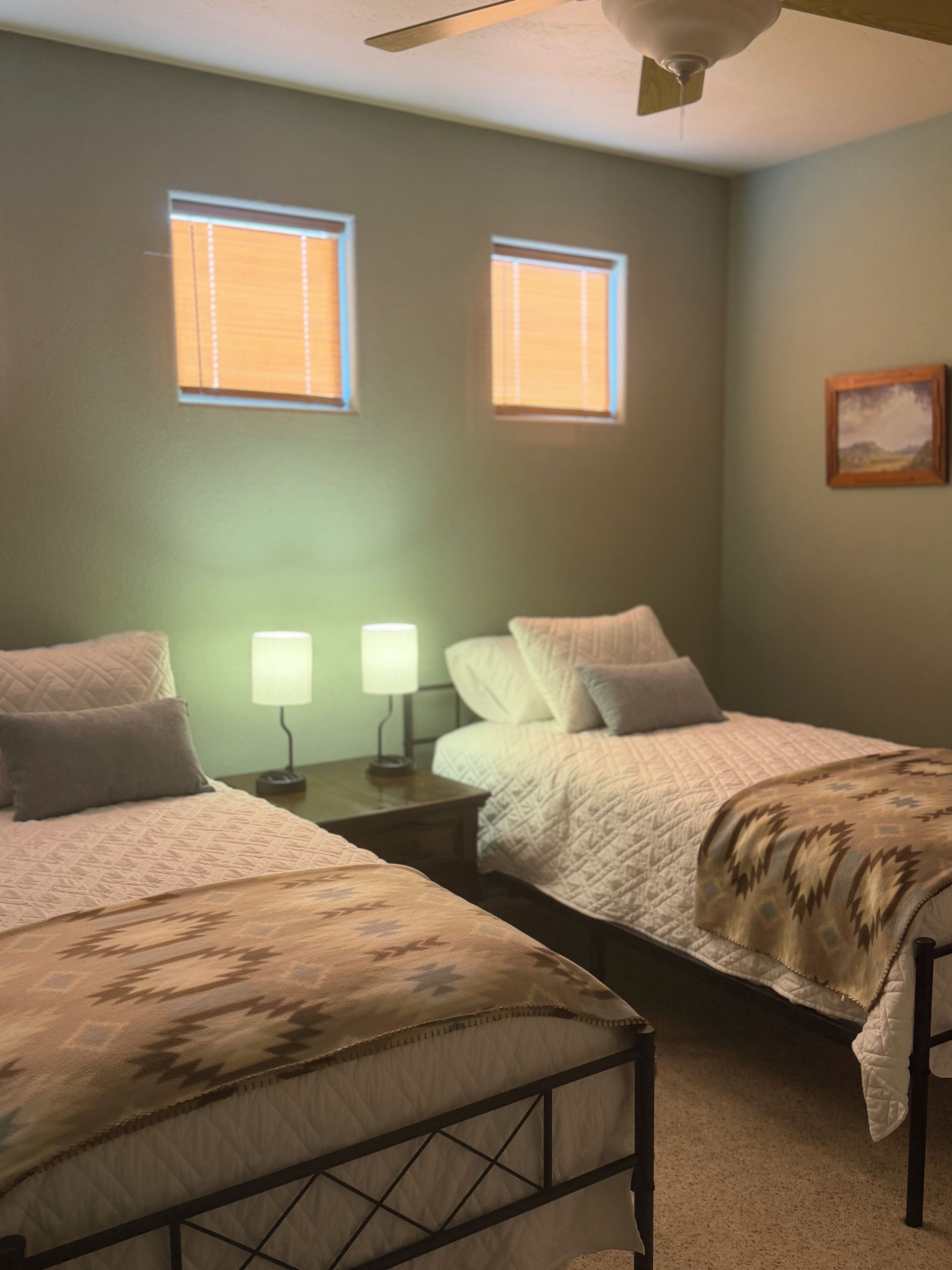 A bedroom with two beds, a ceiling fan, and two windows.