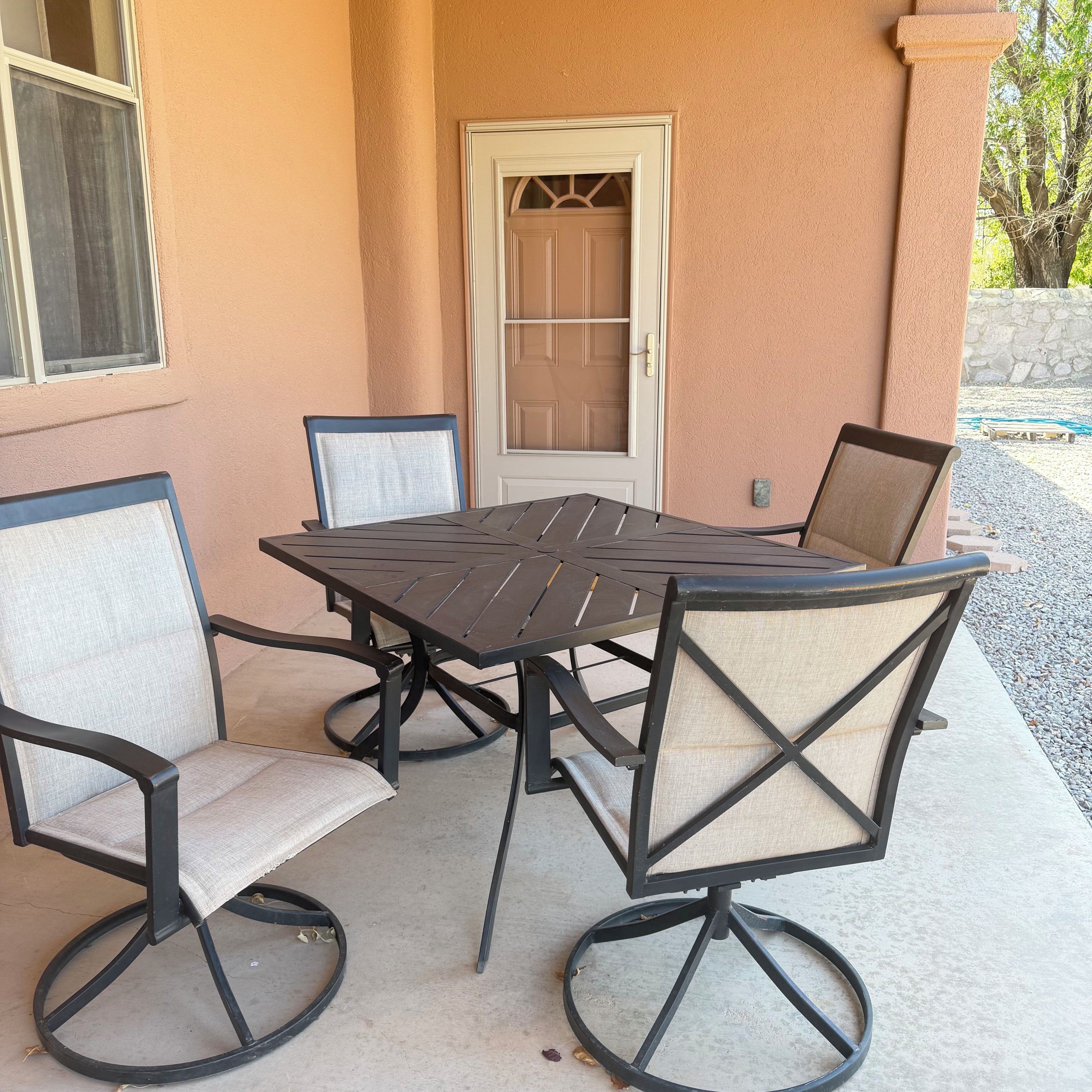 A patio with a table and four chairs, a door, and a stone wall in the background.