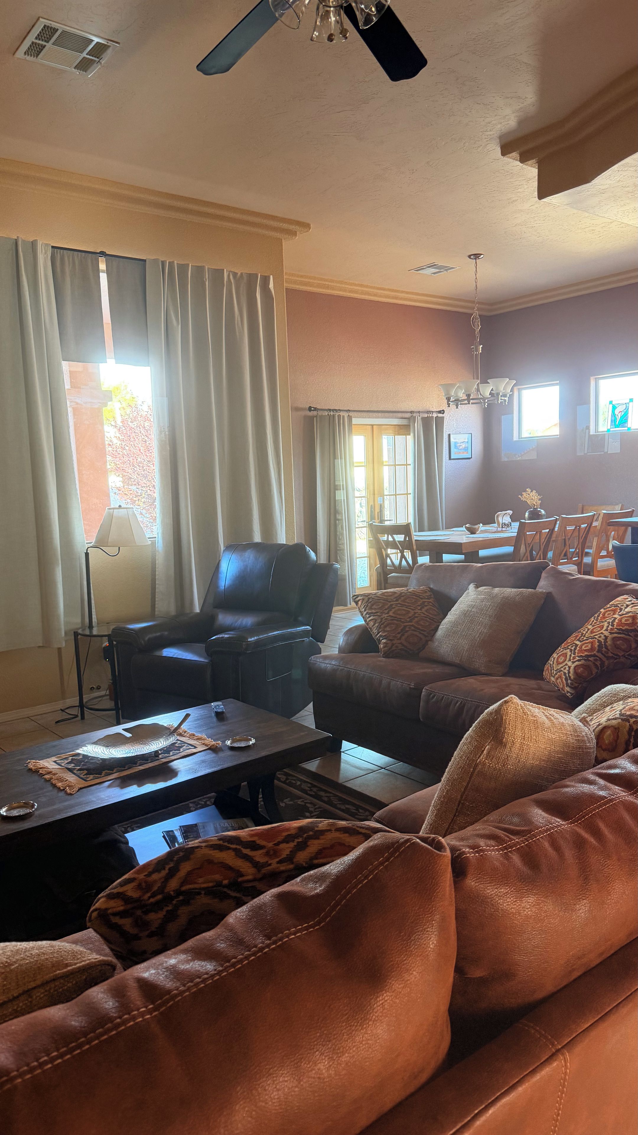 A living room with a leather sofa, a coffee table, a lamp, and a dining area in the background.